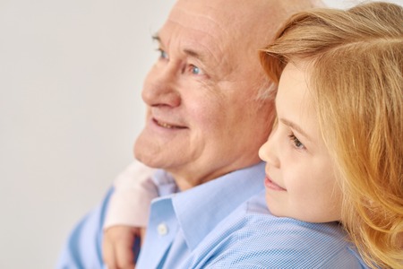 Loking in one direction. Portrait of  pretty small girl lookting somewhere with her loving grandfather  hugging him, isolated on white backgroundの写真素材