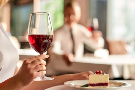 Relaxing time. Close up shot of wine glass hold by woman having dessert at the restaurant.の写真素材