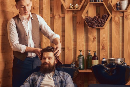 Skillful man. Cheerful barber holding towel and drying hair of his client with it  while doing his jobの写真素材
