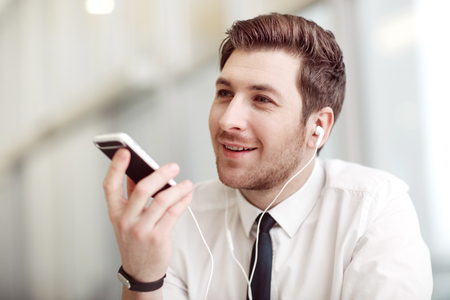 Modern way of life. Handsome cheerful business man holding cell phone and smiling while listening to musicの写真素材