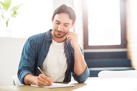 Materialize your thoughts. Pleasant handsome man sitting at the table and holding pen while making notesの写真素材