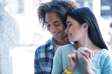 Nude feelings. Pleasant content loving couple sitting near window and drinking coffee while expressing loveの写真素材