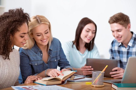 Studying in pairs. Concentrated and smiling students sitting together at the table and doing some tasks during their studying.の写真素材