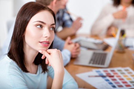 Dreaming. Smiling and charming young woman sitting at the table while dreaming and thinking about her futureの写真素材