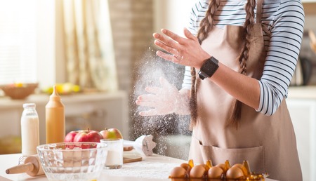 Involved in process. Pleasant woman standing near table and holding flour while cooking in the kitchenの写真素材