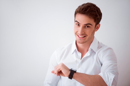 Smart device. Joyful delighted smiling man using his smart watch  while standing isolated o white backgroundの写真素材