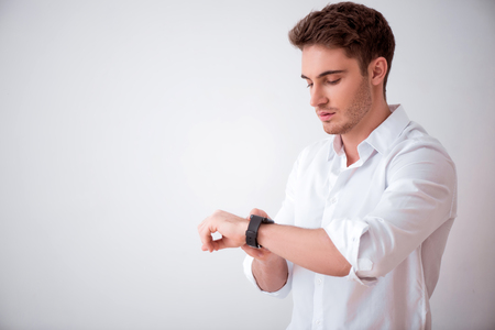 Open up new technologies. Pleasant handsome man using his smartwatch while standing isolated on white backgroundの写真素材