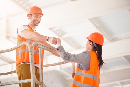 Gentleman. Generous man in a hardhat helping a cheerful woman to go up higherの写真素材