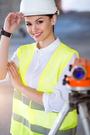 Always prepared. Cheerful and smiling young engineer standing near a geodetic level and looking at a cameraの写真素材