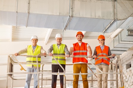 Ready.  Smiling cheerful team of architects standing on a manual fork-lift being in construction worksの写真素材