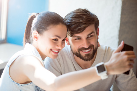Time for selfies. Positive and cheerful modern young woman and man using a cell phone to make a photo togetherの写真素材