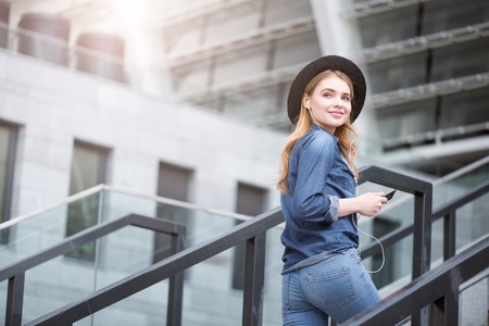 Favorite song. Cheerful and delighted young woman listening to music using her smartphone and...