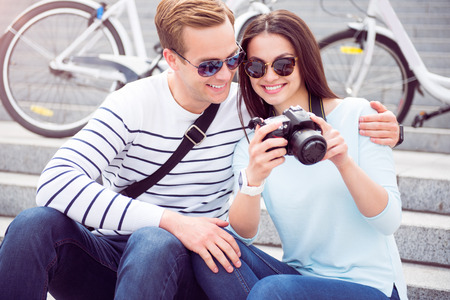 Nice shot. Happy young woman in sunglasses showing photos on the camera to a contented young man...
