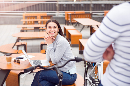 Nice to meet you. Confident young woman with a charming smile sitting and using a laptop while talking to a man sitting on a bikeの写真素材