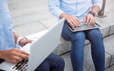 World of technologies. Cropped image of two young people using a digital tablet and a laptop while sitting on the stairs outdoorsの写真素材