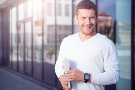 Confident one. Cheerful and smiling young man standing outdoors  while holding some papers and looking at a cameraの写真素材