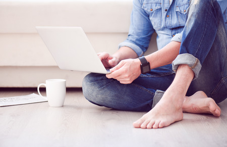 Relaxed surfing in the internet. Close up of legs and hands of a man using a laptop while sitting on...