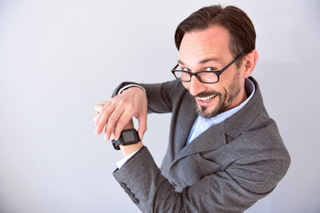 It is very useful. Confident mature man with smile on his face touching and showing a smart watch on his wrist isolated on the grey backgroundの写真素材