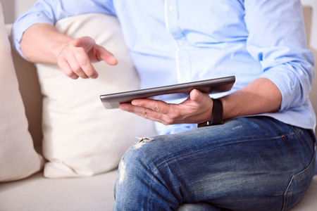 What is new here. Picture of hands of man using a tablet while sitting on the sofa