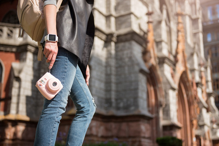Modern tourist. Pleasant woman holding photo camera and having a walk while standing in the street