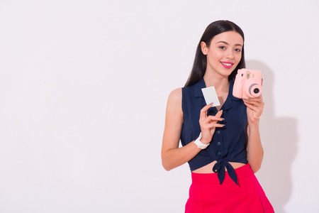 Memory maker. Positive delighted beautiful woman holding photo camera and expressing joy while standing isolated on white backgroundの写真素材