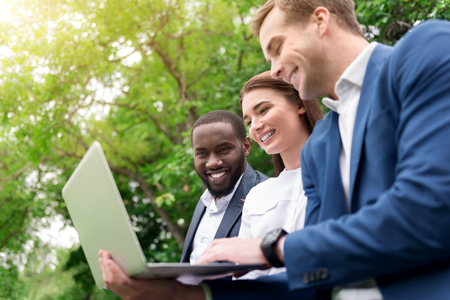Inspired workers. Positive delighted smiling colleagues using laptop and discussing project while expressing joyの写真素材