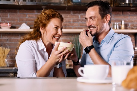 As sweet as sugar. Joyful woman looking at her man and holding a bowl with strawberries