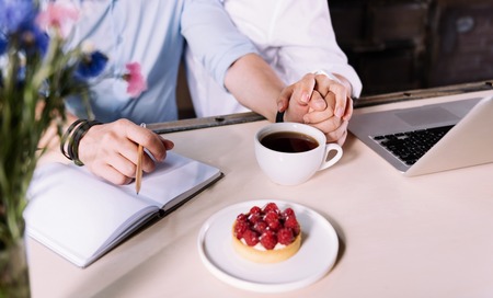 Tenderness of the touch. Close up of couple holding hands on the table with a cup of coffee and a...