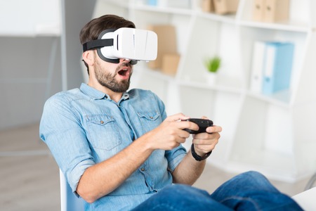 My favorite activity. Pleasant handsome delighted man sitting in the chair and wearing virtual...