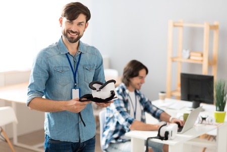 Work with positivity. Positive handsome delighted man holding virtual reality device and standing in...