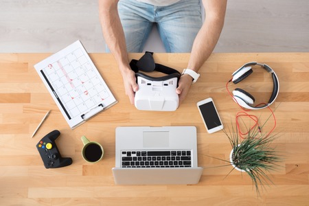 My workplace. Pleasant man holding virtual reality glasses and sitting at the tableの写真素材