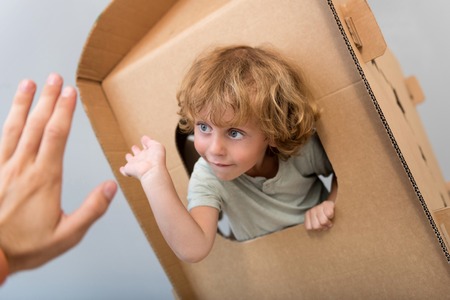 Take it. Captivating little boy sitting in the carton rocket and giving five to a hand of a man...