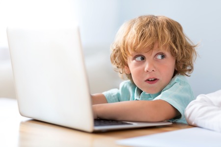 I can do it. Close up of an amiable funny little boy looking aside while using a laptop and sitting...