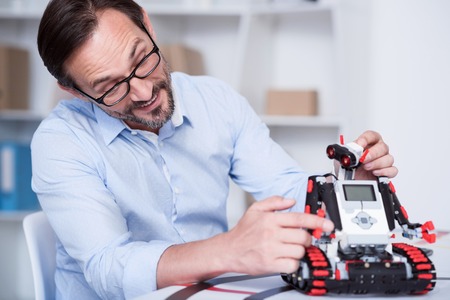 Fun time. Attractive Caucasian man tickling a robot as a pet