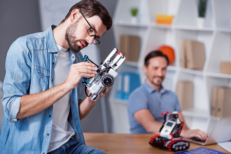 Try it out. Pleasant concentrated man sitting at on the table and testing robot while his colleague...