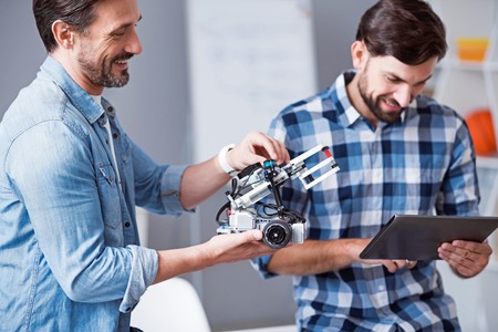 Rise your mood. Positive smiling senior man holding robot while his colleague using tabletの写真素材