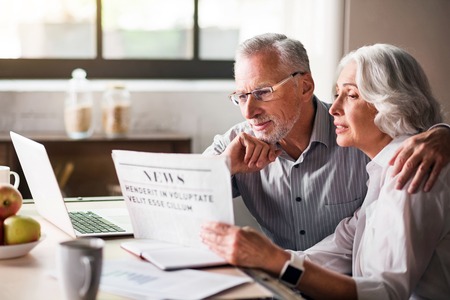 Family life. Retired husband and wife hugging each other at the dinner table while sharing the news from the mediaの写真素材