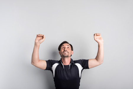 Achieve success in sport. Positive delighted bearded man smiling and pretending doing exercises on the horizontal bar while standing isolated grey backgroundの写真素材