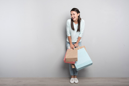 Best way to rest. Cheerful beautiful delighted woman holding packages and looking at you while resting after shoppingの写真素材