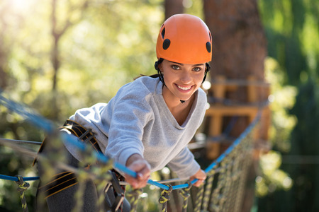 Pleasant climbing activities. Active confident beautiful woman standing on the rope way and leaning forwards while spending her time in high wire parkの写真素材