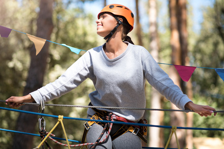 Enjoying the atmosphere. Nice delighted well built woman being high above the ground and looking to the right while doing her high ropes courseの写真素材