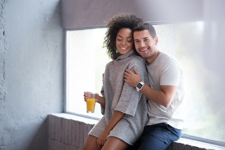 Hold me closer. Sweet young happy couple enjoying their love while embrace and spending morning with a glass of juice together.の写真素材