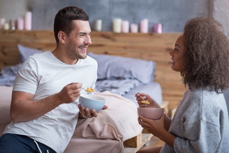 Young happy sweet couple having their breakfast together while sitting in the bedroom and enjoying their honeymoon.の写真素材