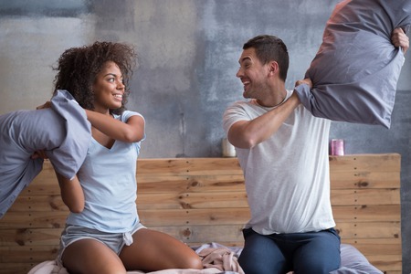 Morning entertainments. Smiling happy young couple fighting with pillows while having fun enjoying their morning in bed.の写真素材