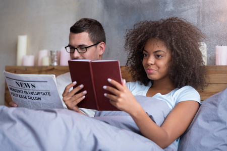 More information. Young sweet lovely couple reading books and newspapers together while lying in bed on their honeymoon.の写真素材