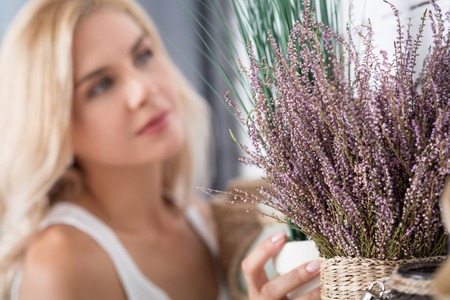 Perfect match. Close up view of fake dry decorative flower on background of pretty blurred blond woman.の写真素材