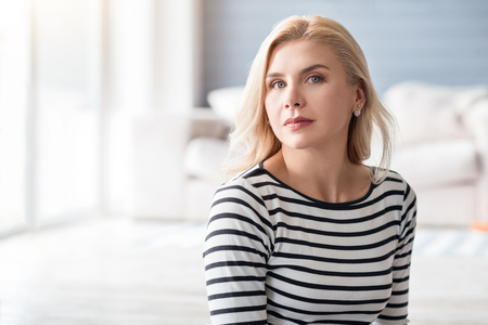 Feeling confident. Good-looking serious blond woman on background of white decorated room.の写真素材