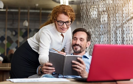 Giving number. Pretty ginger woman standing near bearded man holding notebook and making notes there.の写真素材