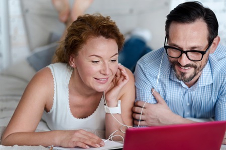 Fascinating video. Close up of man and woman lying on bed watching information on laptop and sharing earphones.の写真素材