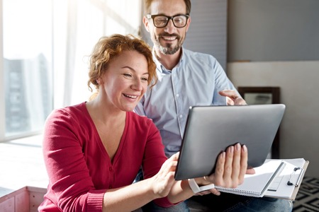 Video conversation. Smiling ginger woman standing and holding tablet near handsome bearded man.の写真素材